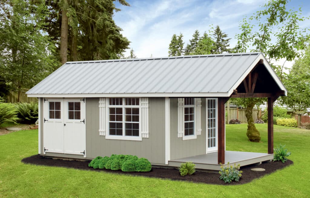 gray gable cabin with metal roof white trim and front porch surrounded by mulch garden