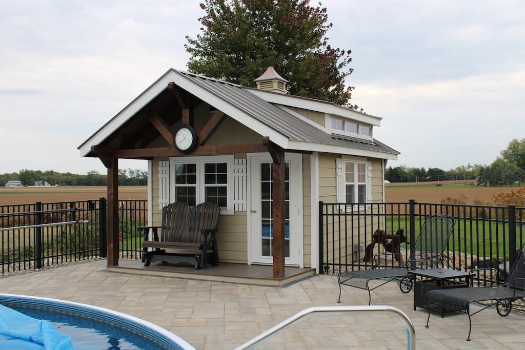 tan shed with white trim and gray roof and overhang by pool