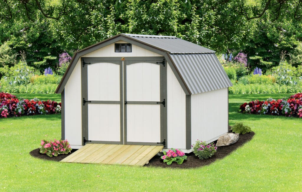 white barn style shed with dark gray trim and metal roof with wooden ramp leading up to double doors